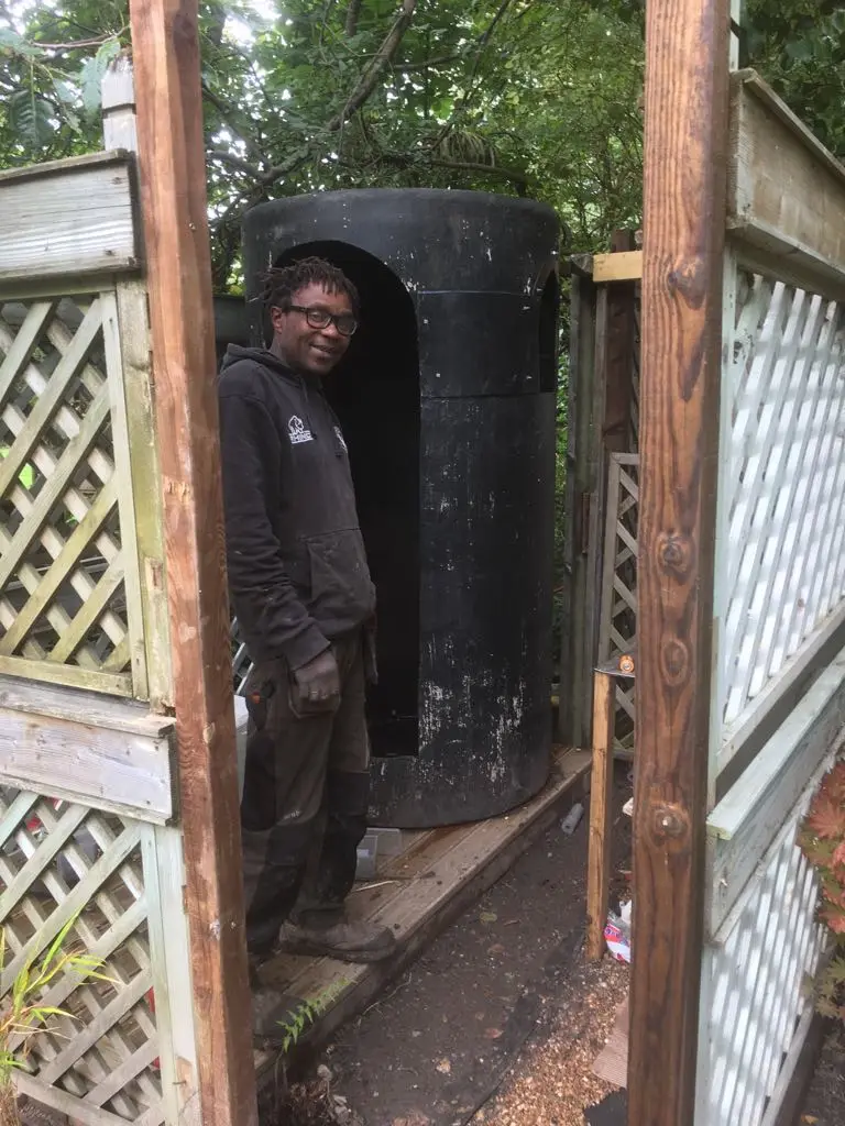 Tom Nyamunda on site in work clothes beside a water tank in a fenced garden
