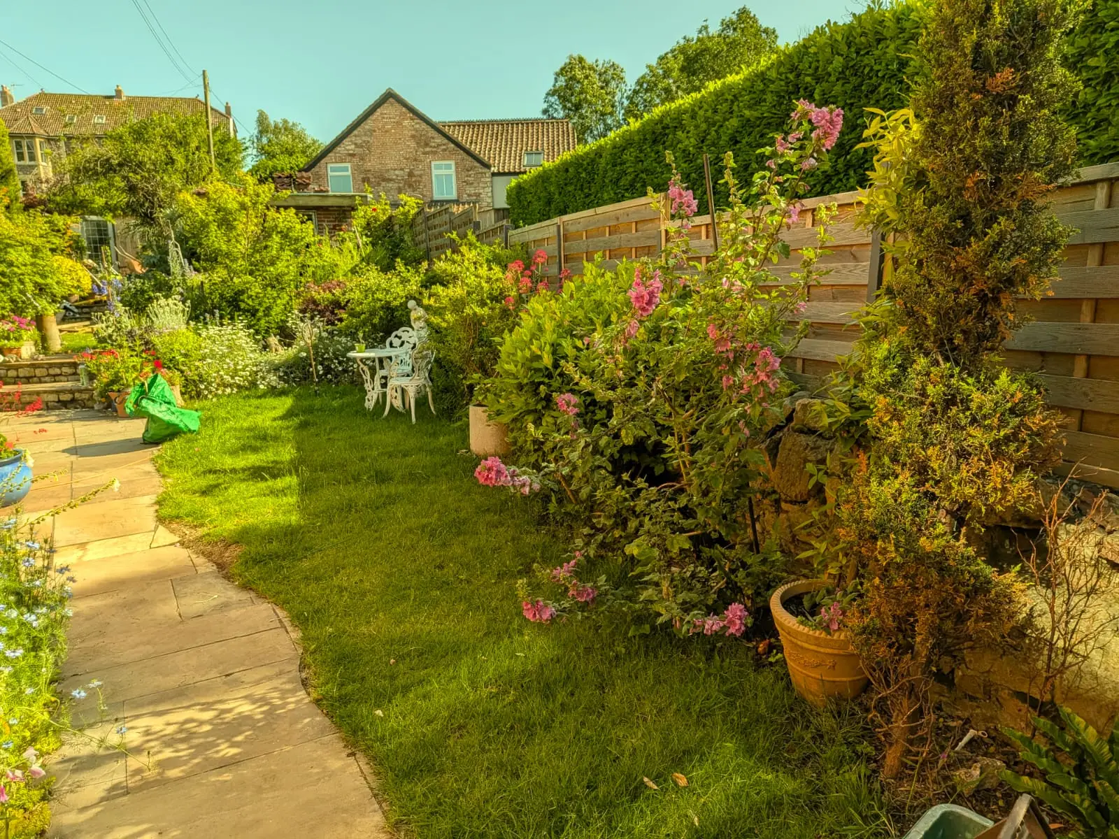 Cottage garden with a sandstone path, a cut lawn and deep planted borders against a fence