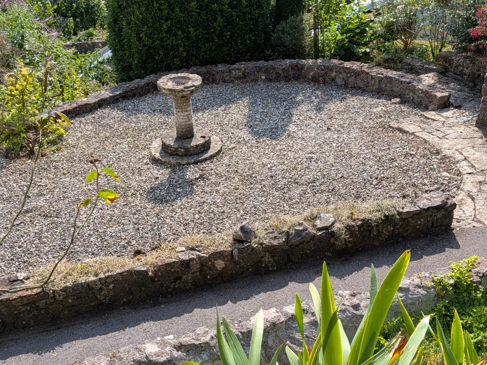 Gravel garden edged in natural stone with a reclaimed staddle stone set at the centre
