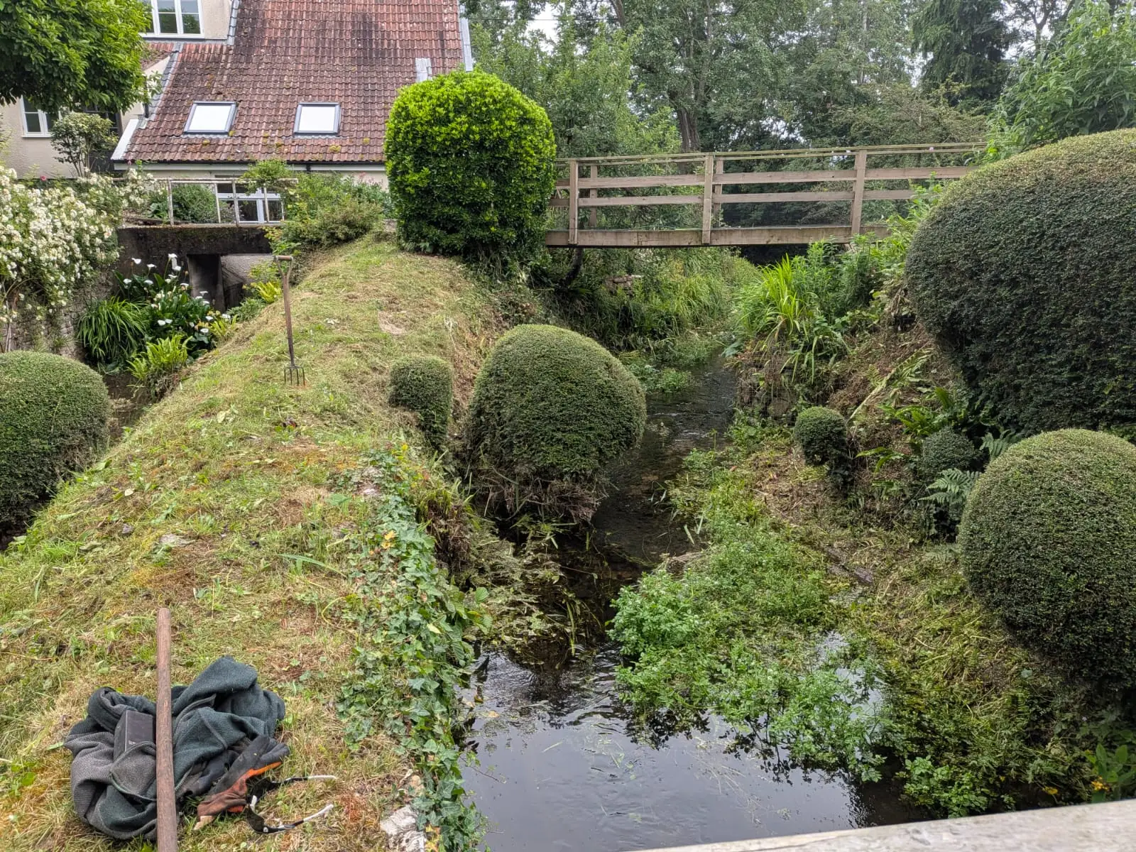 Stream bank cut back and cleared, with clipped box topiary balls either side of the water