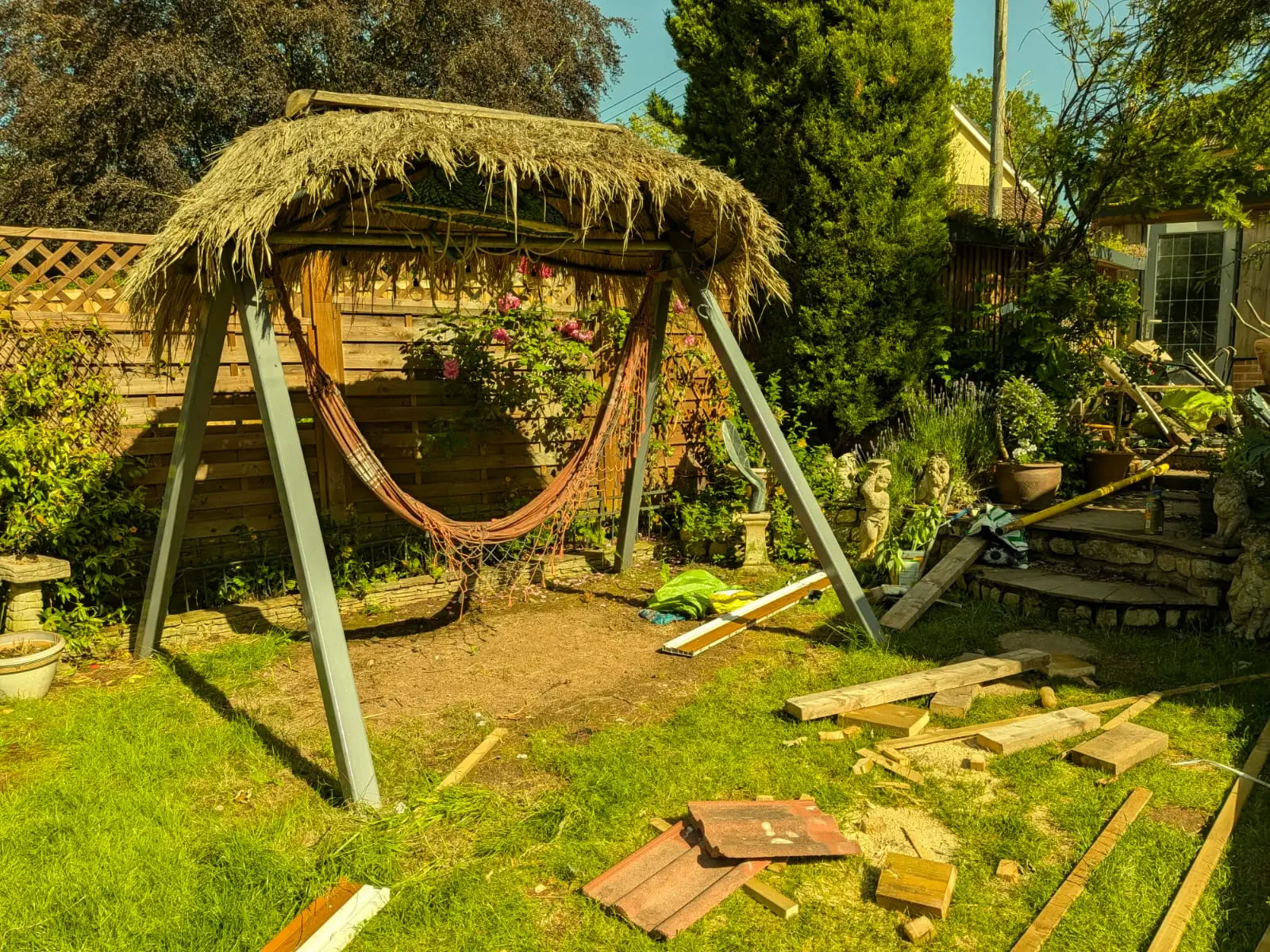 Timber swing frame with a thatched roof built onto a lawn, hammock slung underneath