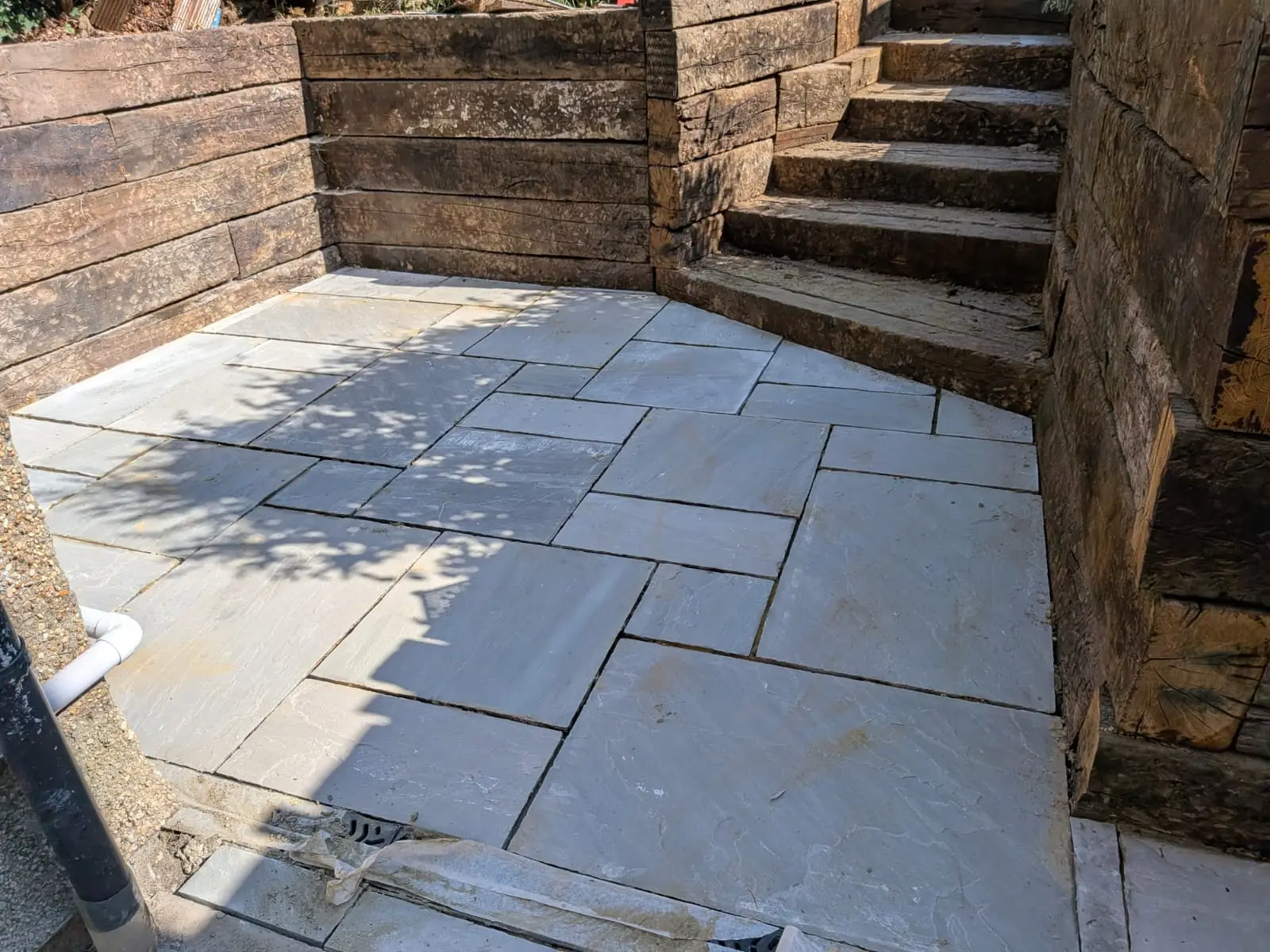 Grey Indian sandstone patio laid in a random pattern inside a railway sleeper retaining wall
