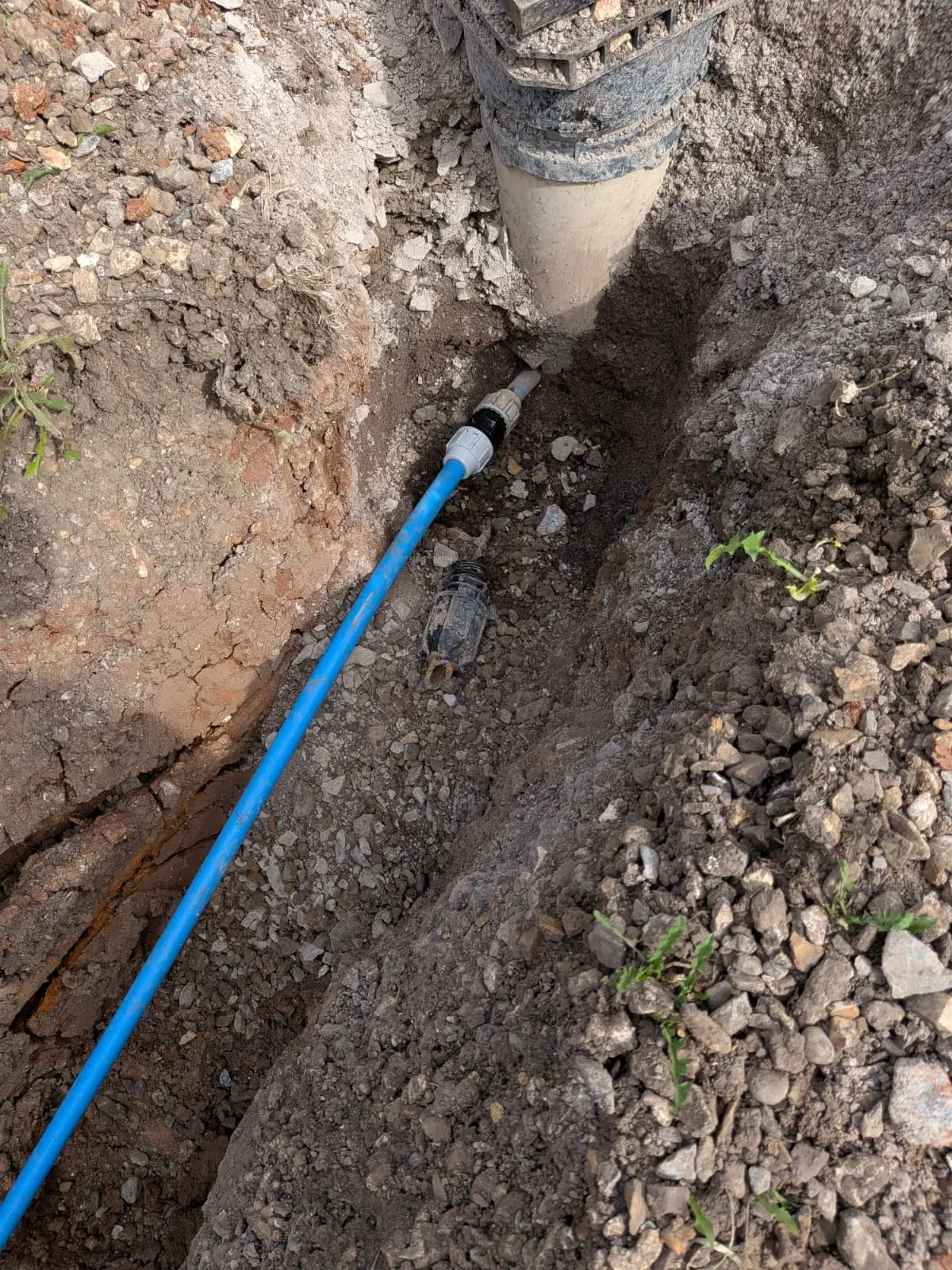 New blue MDPE water main laid along the bottom of a trench beside a drainage stack